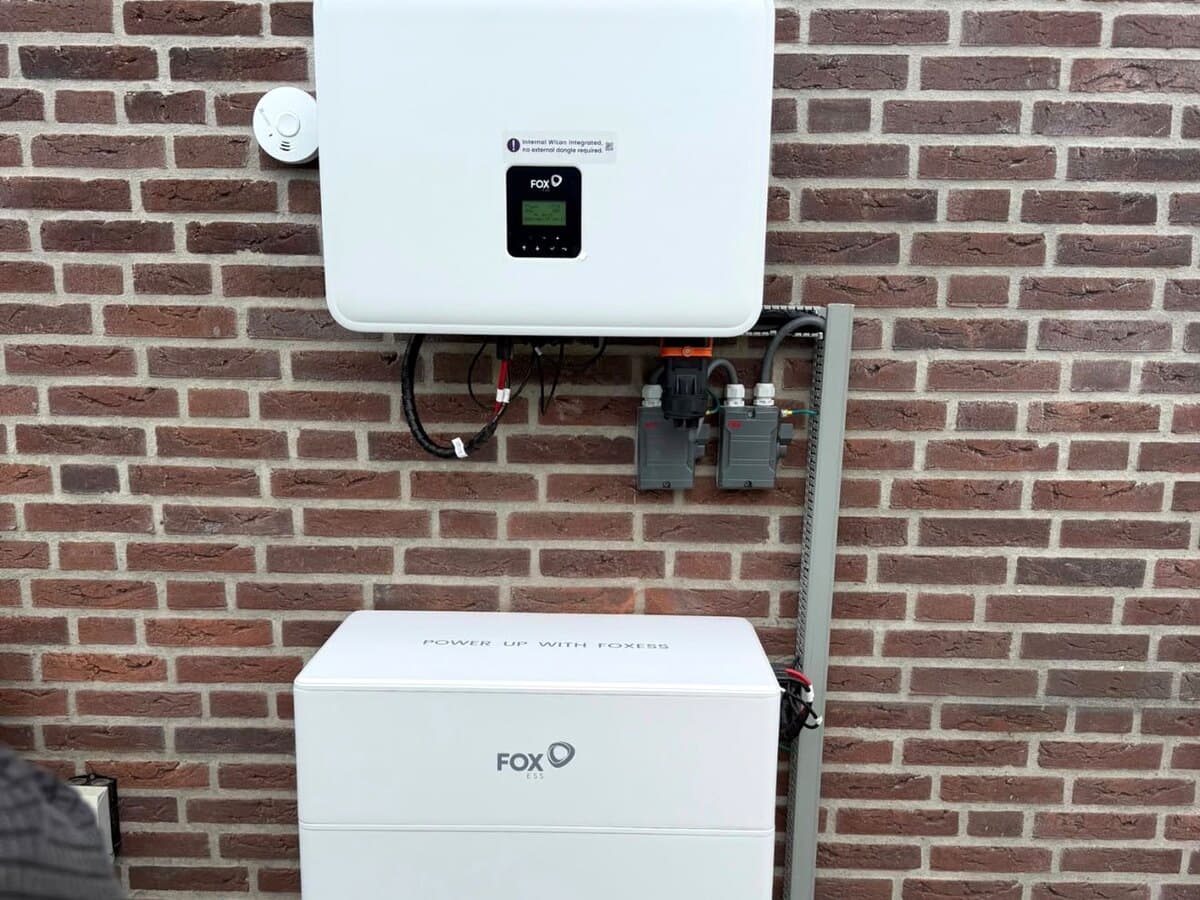 Buitenopstelling met omvormer en batterijmodules tegen een gemetselde gevel